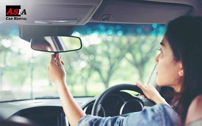 a lady adjusting a rear view mirror
