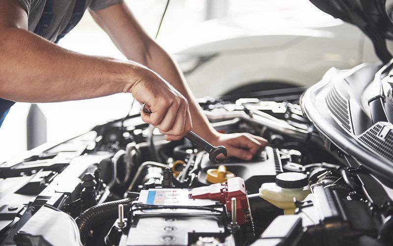 Mechanic fixing car engine to manage vehicle maintenance costs